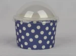 "A medium-sized ice cream cup adorned with white polka dots on a navy blue background, featuring a transparent dome lid, from www.jcpackaging.net."