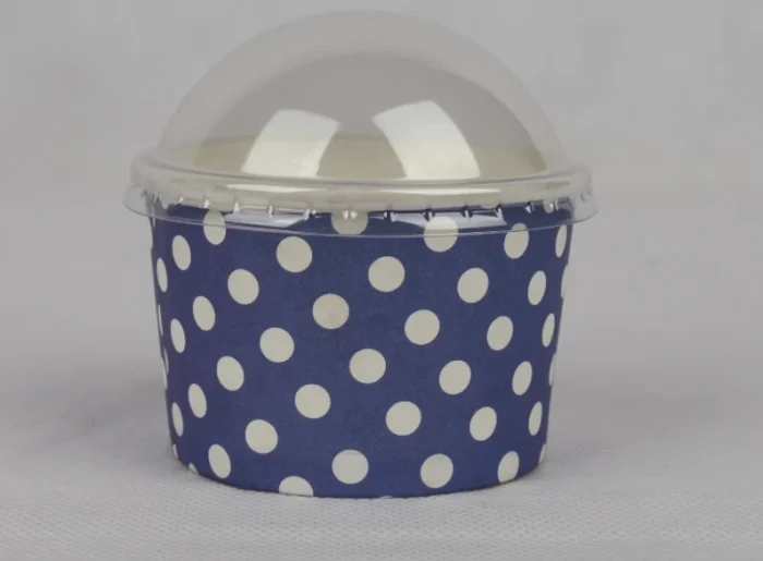 "A medium-sized ice cream cup adorned with white polka dots on a navy blue background, featuring a transparent dome lid, from www.jcpackaging.net."