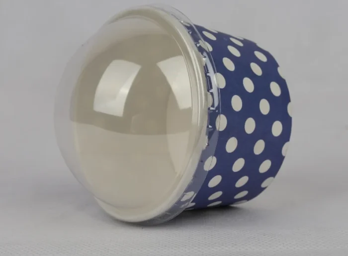 "A medium-sized ice cream cup adorned with white polka dots on a navy blue background, featuring a transparent dome lid, from www.jcpackaging.net."