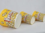 "A cascading arrangement of yellow popcorn buckets with red 'Popcorn' text and popcorn graphics from www.jcpackaging.net."