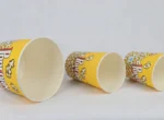 "Three yellow popcorn buckets from www.jcpackaging.net, playfully tumbled to display the popping design."