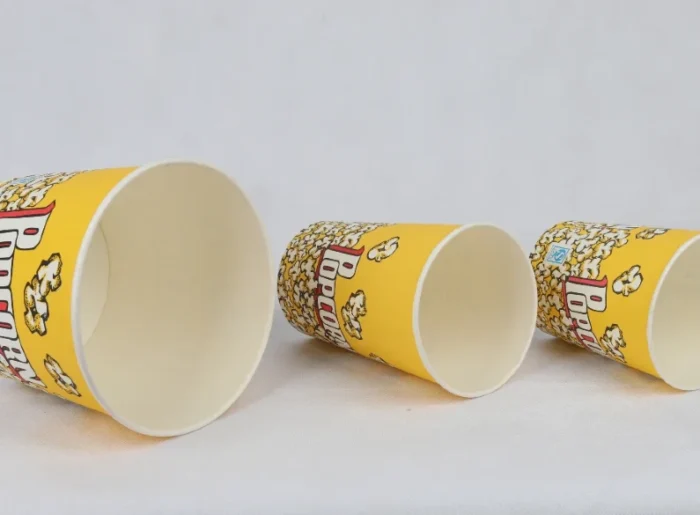 "Three yellow popcorn buckets from www.jcpackaging.net, playfully tumbled to display the popping design."