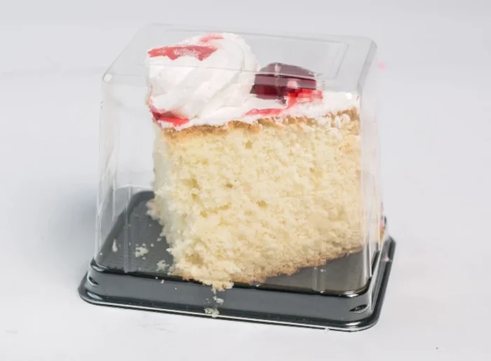 "Single slice of creamy vanilla cake with strawberry topping, encased in JC Packaging's crystal-clear, durable cake slice packaging, emphasizing both protection and presentation."